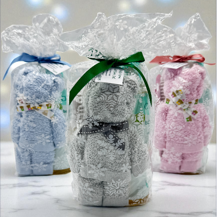 Three baby gifts in seasonal print see through gift bags with ribbons on a marble surface.
