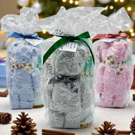 Three gift ready wrapped baby stocking gifts with decorative ribbons on a table with Christmas decorations in the background.