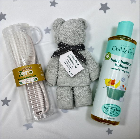 Childs Farm baby bath set with teddy bear facecloth , brush and comb set, and a childs farm baby bedtime bubbles bottle on a star-patterned background