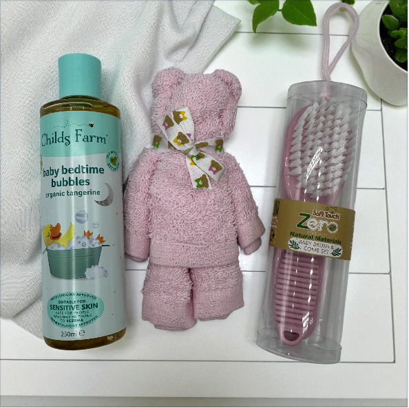 Childs Farm baby bedtime bubbles, pink face cloth in the shape of a teddy bear, and Zero Baby brush set on a white surface.