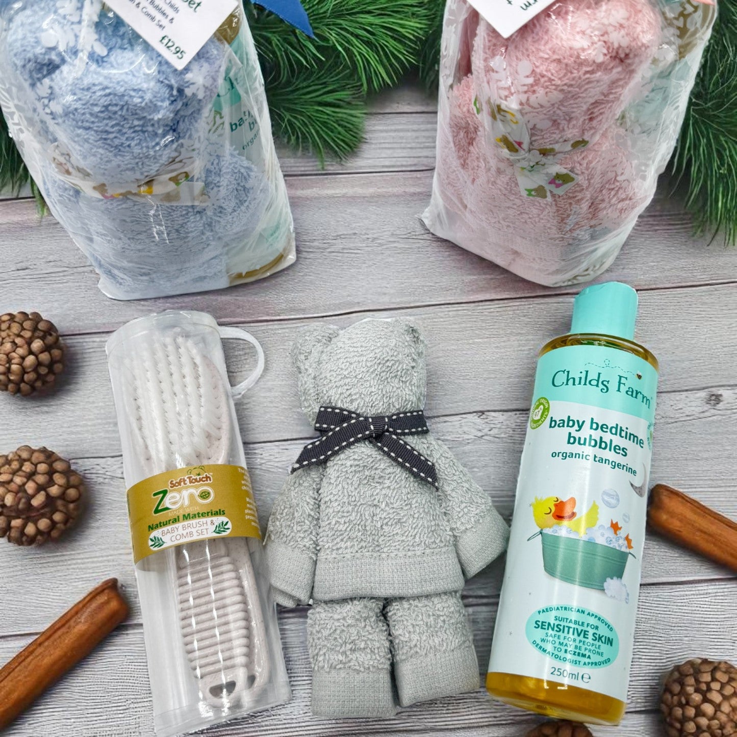 Baby care products including an Eco-friendly Brush and Comb Set, a face cloth rolled into the shape of a teddy Bear, and a bottle of Childs Farm baby bedtime bubbles on a wooden surface with decorative elements.