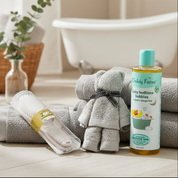 Baby care products including an Eco-friendly Brush and Comb Set, a face cloth rolled into the shape of a teddy Bear, and a bottle of Childs Farm baby bedtime bubbles on a wooden surface with decorative elements.