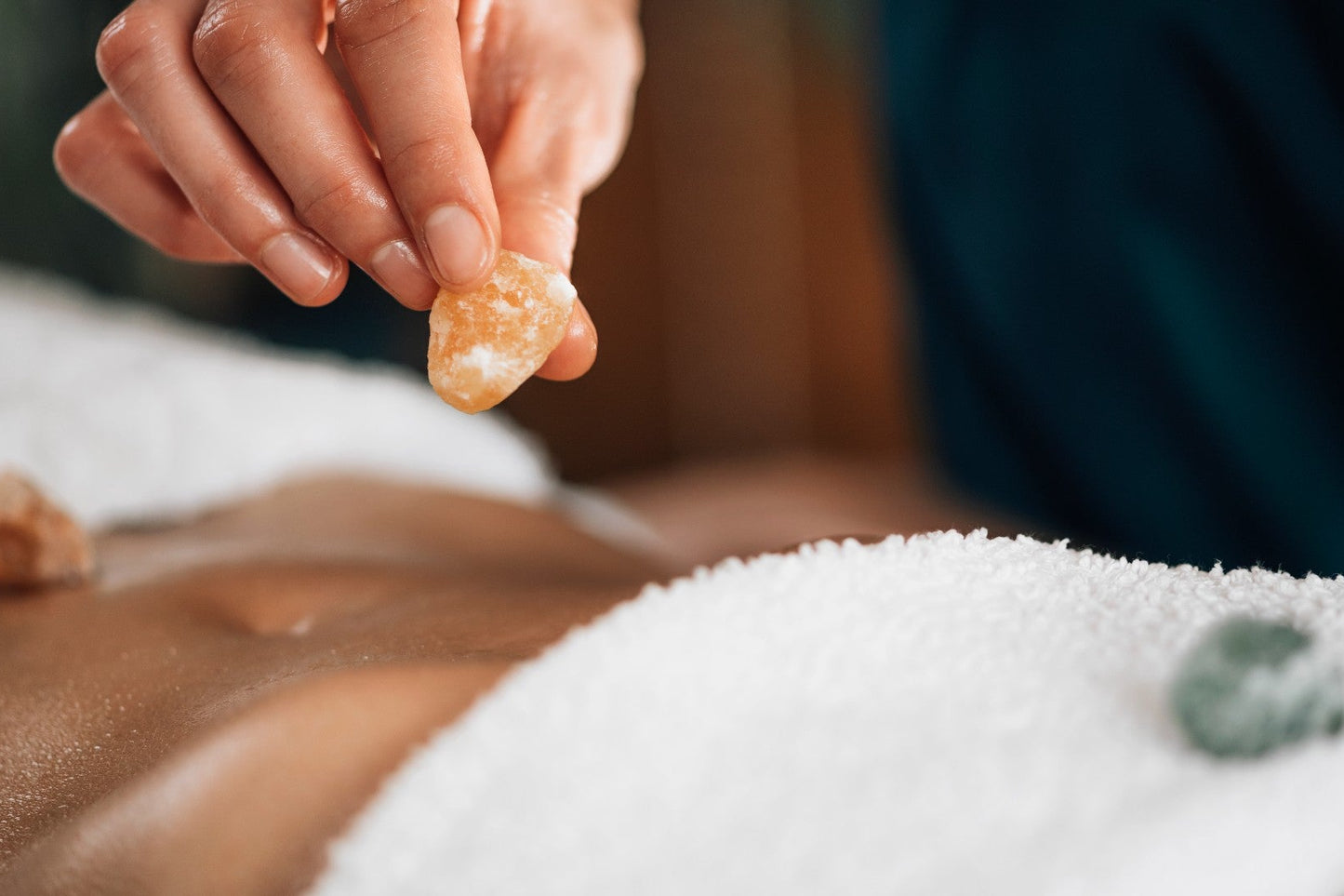 Hand applying a small stone to a person's back during a stone therapy session.