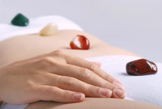 Hand gently placed on a person's abdomen with healing gemstones nearby