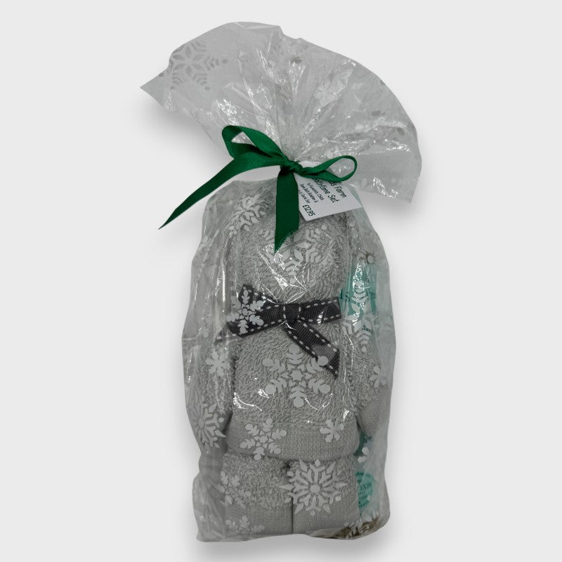 Gift Ready Stocking Filler for a baby, that contains Baby care products including an Eco-friendly Brush and Comb Set, a face cloth rolled into the shape of a teddy Bear, and a bottle of Childs Farm baby bedtime bubbles. All wrapped in seasonal cellophane and tied with a green satin bow. against an off white background