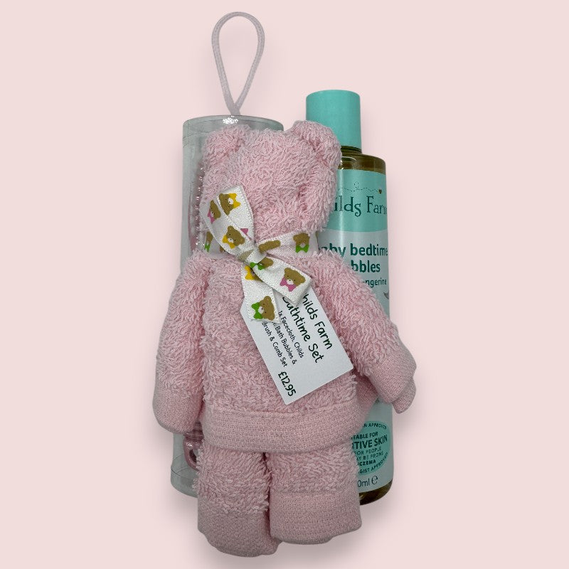 Pink face cloth shaped like a teddy bear with a bottle of baby bath bubbles on a pink background