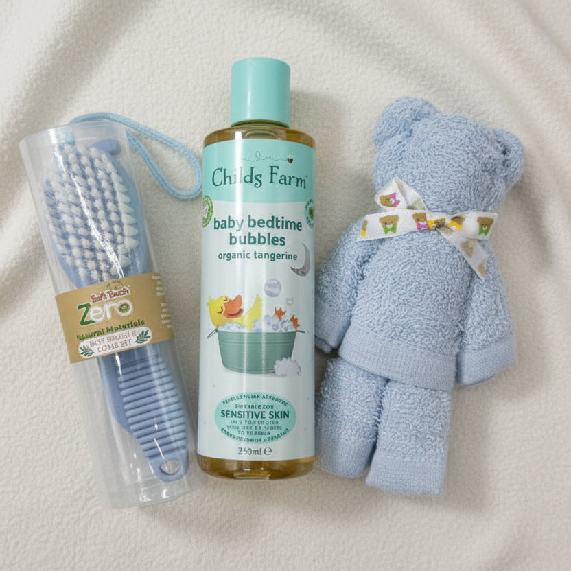 Childs Farm baby bedtime bubbles bottle with a blue face cloth teddy bear and soft touch zero brush and comb set, on a light blue background
