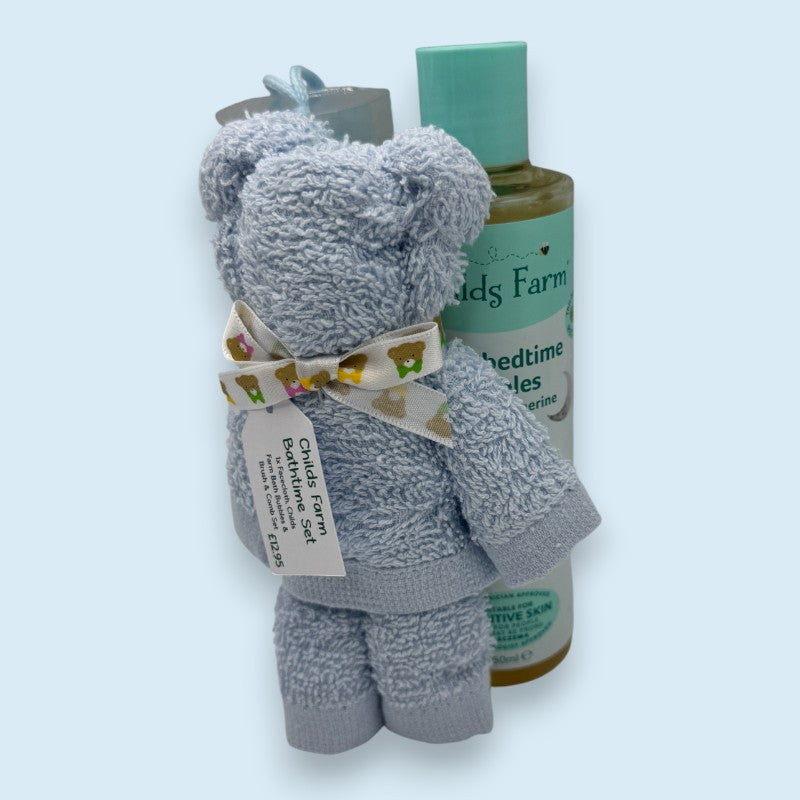 Blue plush wash cloth teddy bear with a bottle labeled 'Childs Farm' on a light blue background