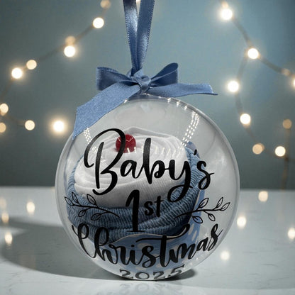 Decorative ornament for baby's first Christmas with text and blue ribbon against a blurred light background.