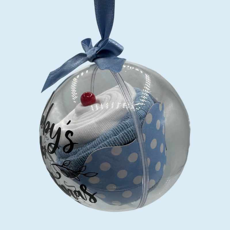Decorative clear fillable "cupcake" bauble with baby clothes  arranged to look like a cupcake and 'Baby's 1st Christmas 2025' text on the bauble with a light blue background