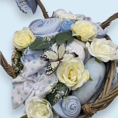 Baby boy gift basket with blue and white baby clothes, white roses, and a butterfly on a white background.
