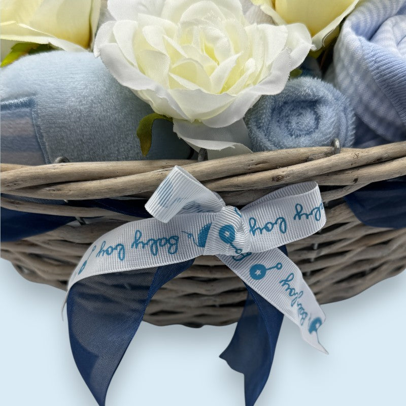 Wicker basket with blue and gray baby items and white flowers on a light background