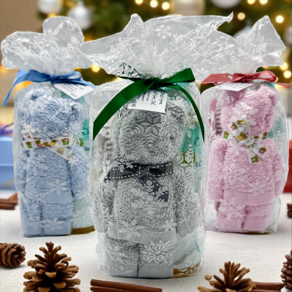 Three gift ready wrapped baby stocking gifts with decorative ribbons on a table with Christmas decorations in the background.