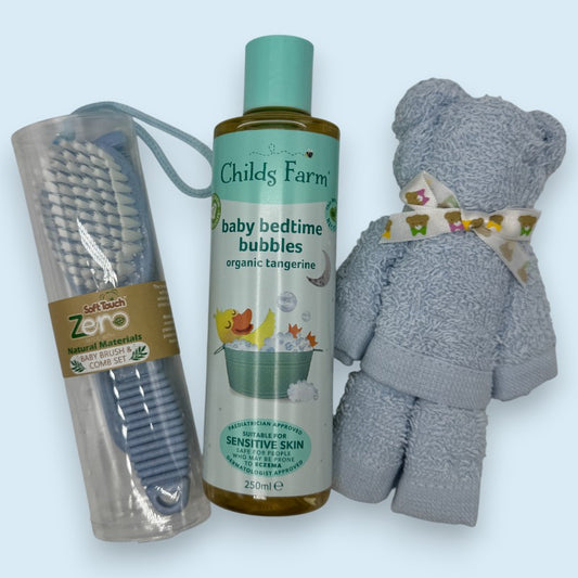 Childs Farm baby bedtime bubbles bottle with a blue face cloth teddy bear and soft touch zero brush and comb set, on a light blue background