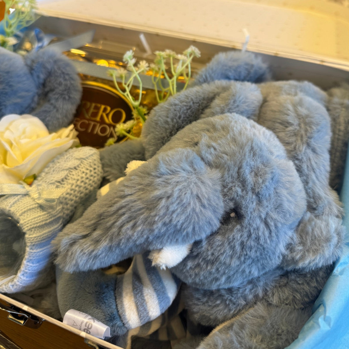 Close-up of soft toys and blue baby booties in a baby gift suitcase