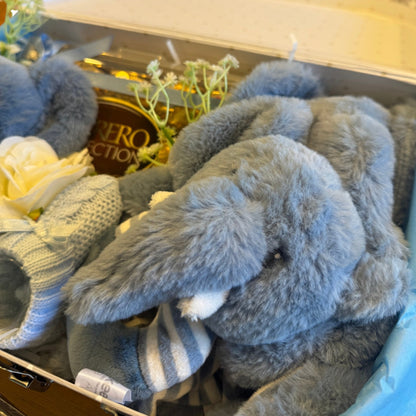 Close-up of soft toys and blue baby booties in a baby gift suitcase
