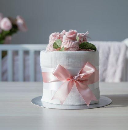 Baby girl mini nappy cake in pink with white muslin, knitted booties, and socks by Love & Tiers
