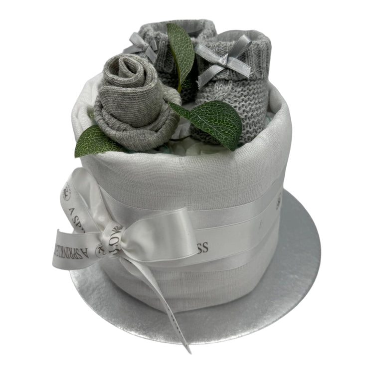 Side view of mini neutral nappy cake with grey knitted baby booties