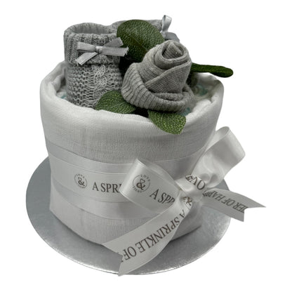 Handmade neutral baby nappy cake with grey knitted booties and white ribbon. with a white background