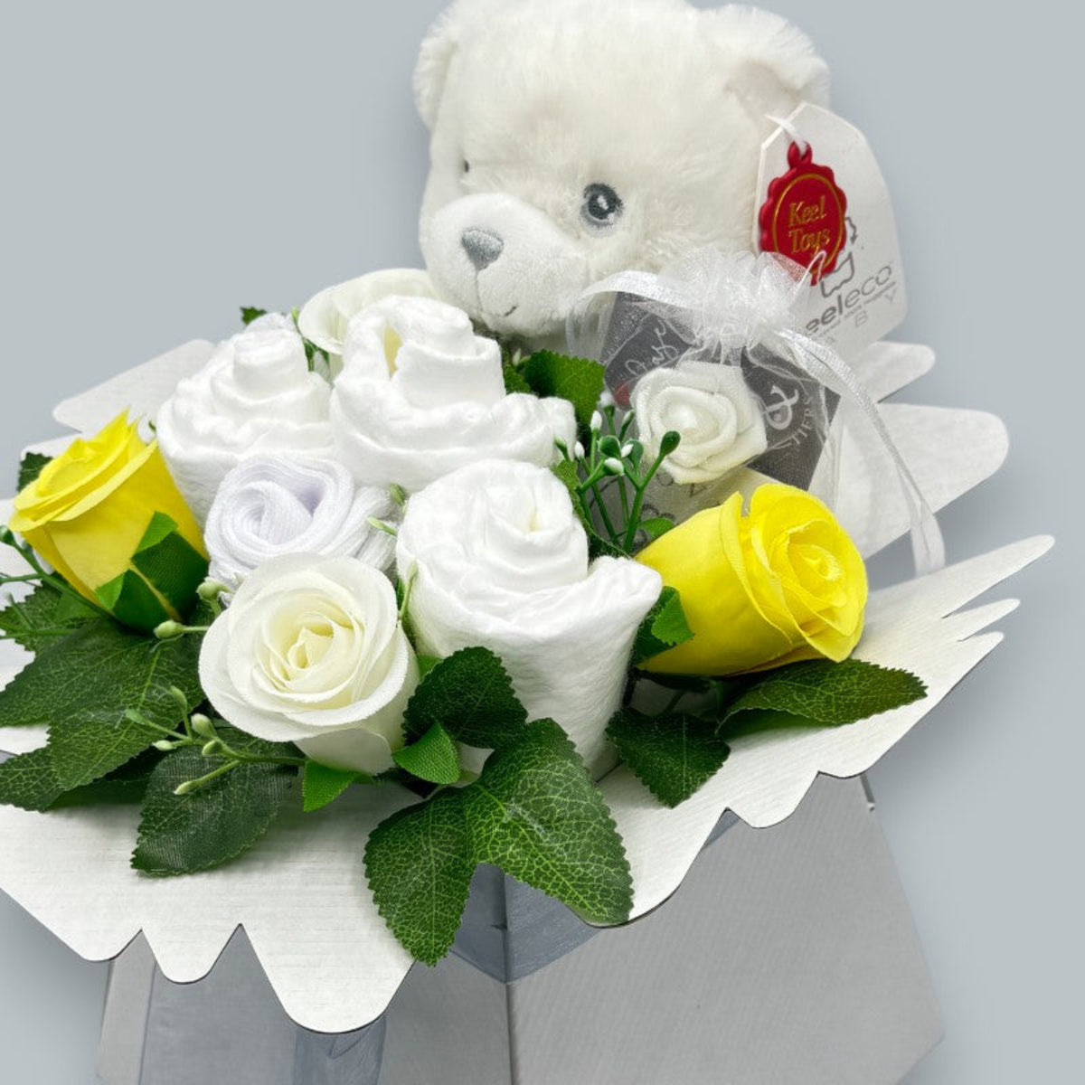Close-up of neutral newborn gift box with nappies, baby socks, yellow roses and Keeleco teddy bear