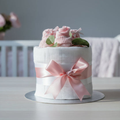 Pink nappy cake with knitted booties styled in a soft nursery setting