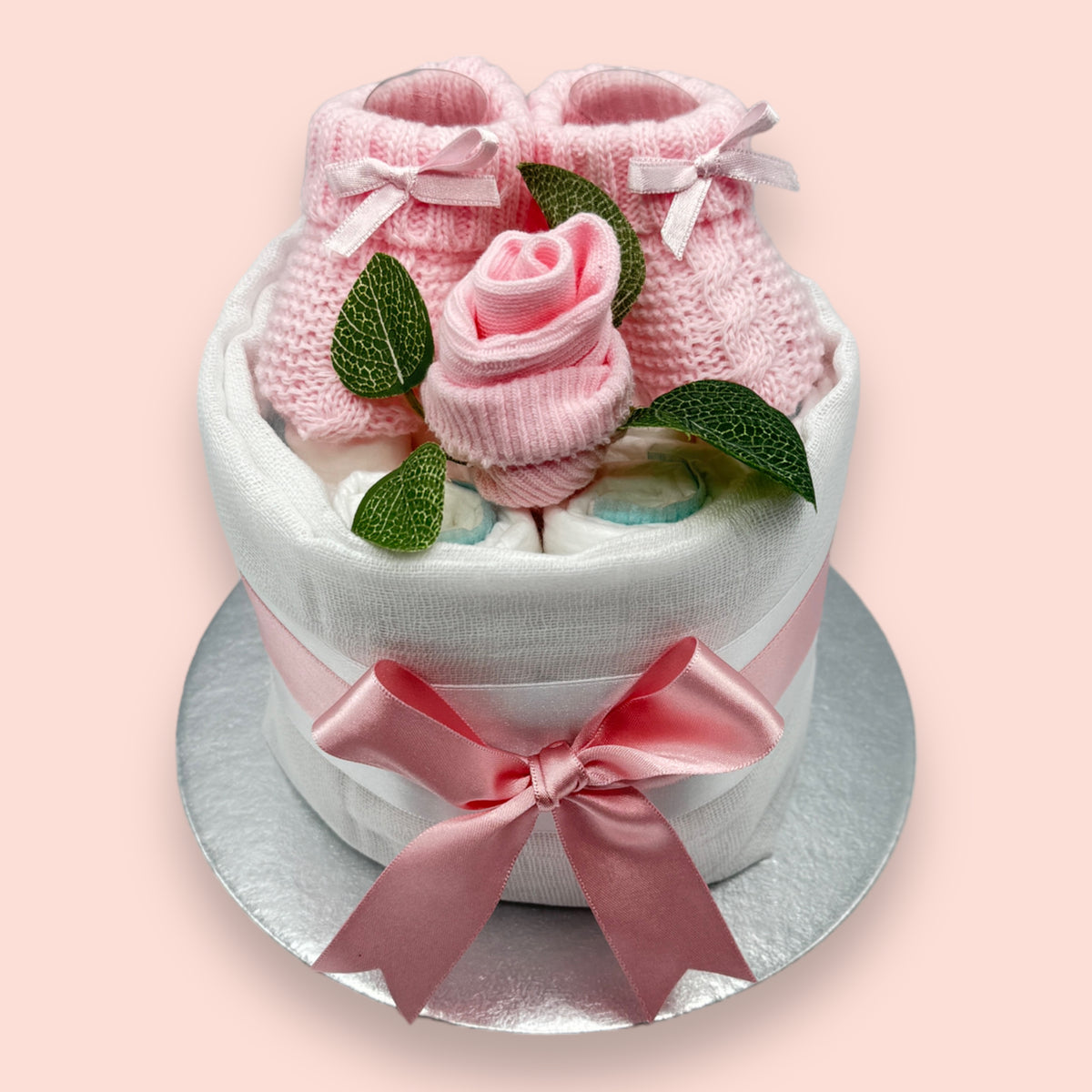 Pink baby nappy cake showing Pampers nappies, knitted booties and baby sock rose