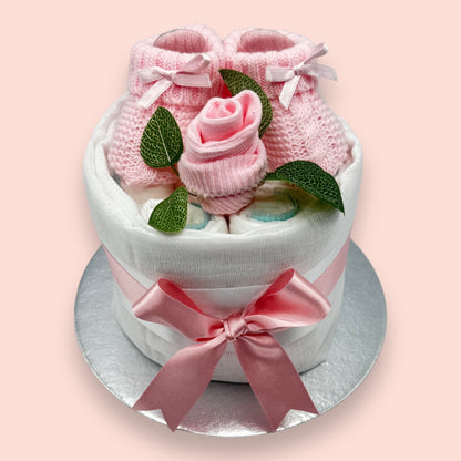 Pink baby nappy cake showing Pampers nappies, knitted booties and baby sock rose