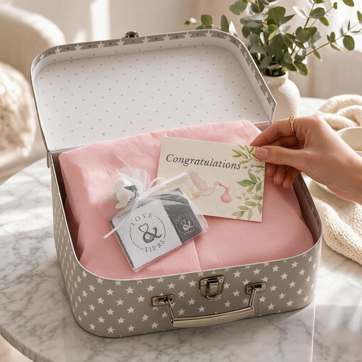 Pink baby gift suitcase being opened to reveal a Love & Tiers congratulations card