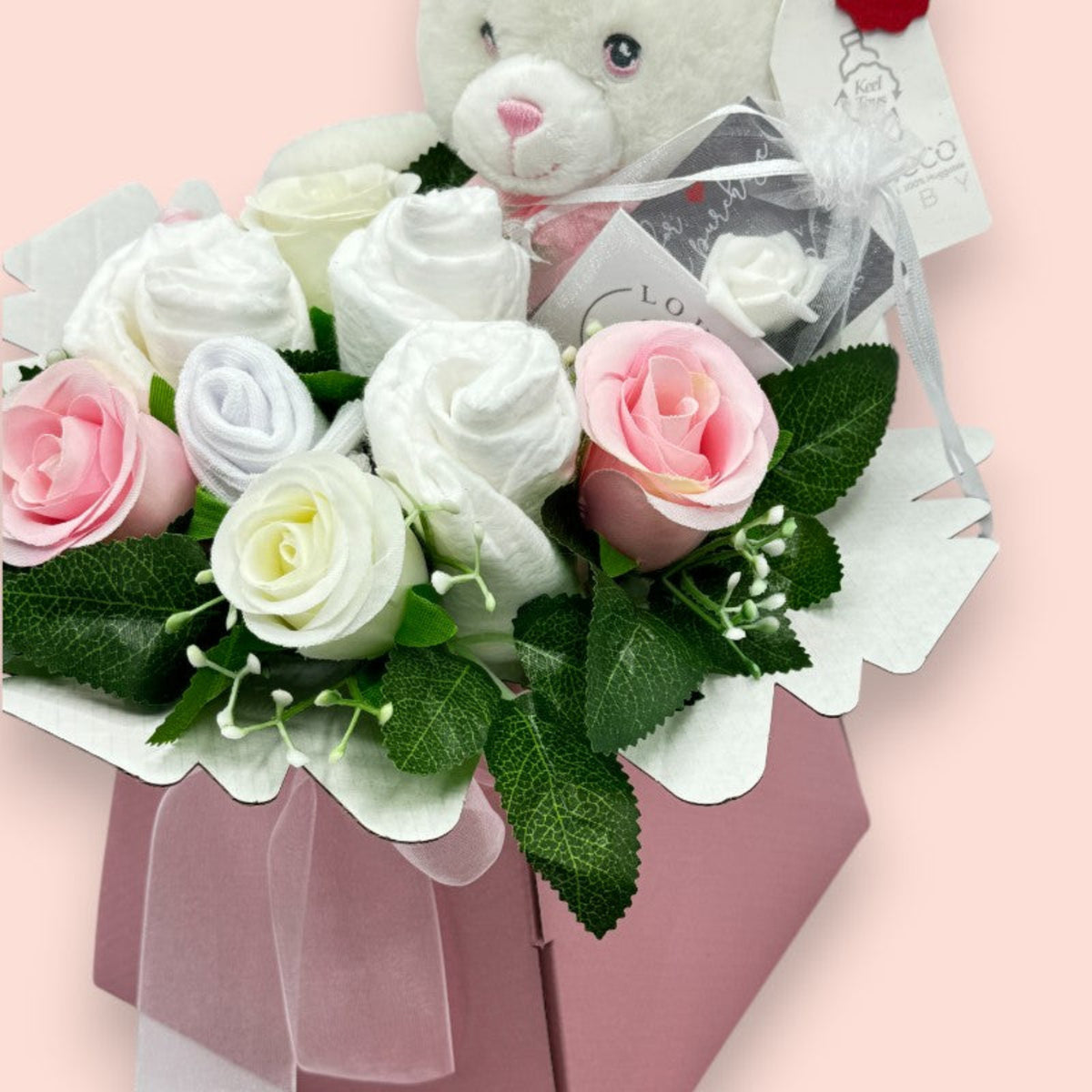Close-up of pink newborn gift box with nappies, baby socks, roses and Keeleco teddy bear